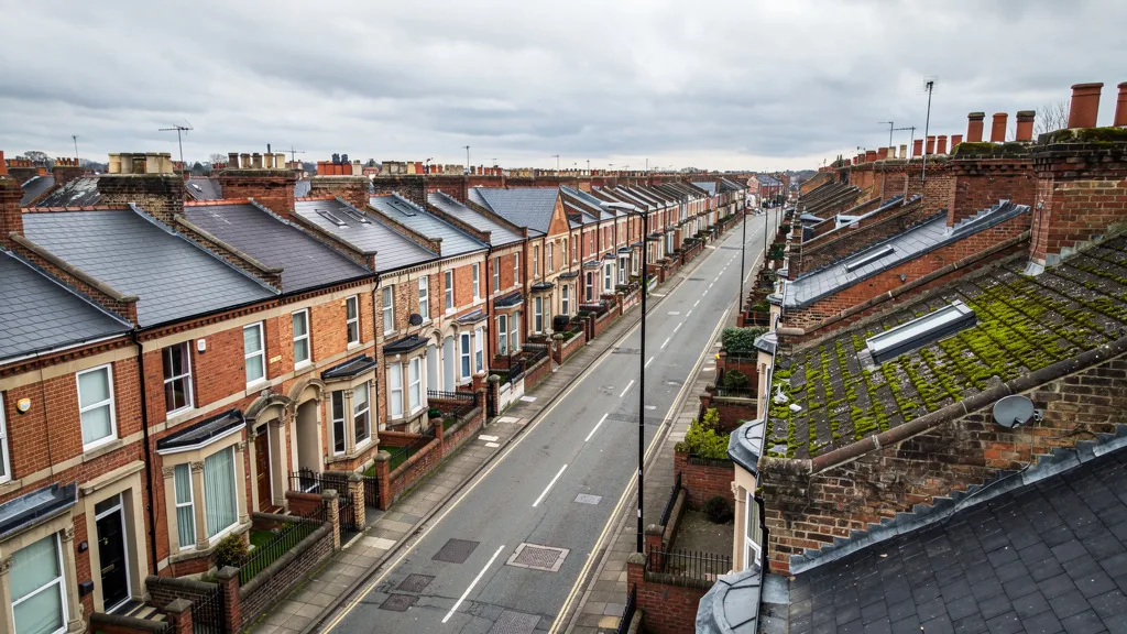 Aerial view of a dense Victorian terraced street under overcast sky, red-brick houses with slate roofs arranged in tight rows, muted grey and terracotta tones, no people visible.