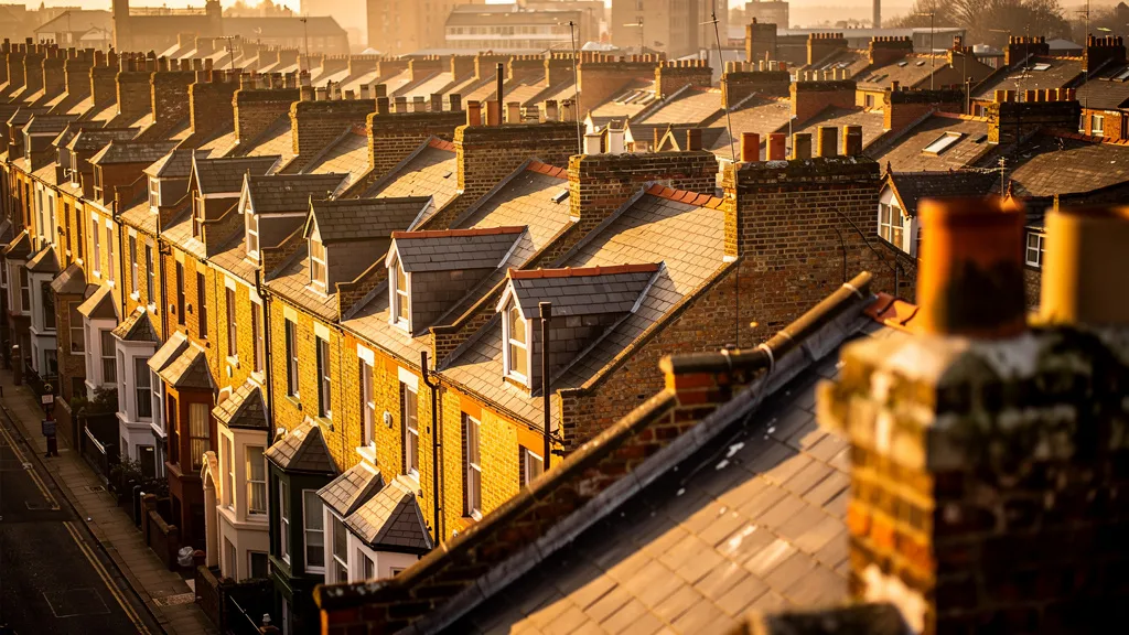 Aerial view of Victorian terraced houses in a northern English city at golden hour, warm amber light casting long shadows across ochre and terracotta brick rooftops, urban density visible in the dense row of properties.
