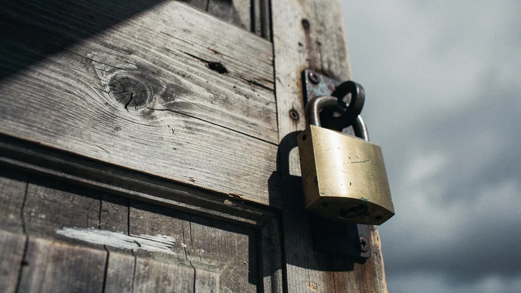 Heavy wooden door with brass padlock slamming shut, photographed from below against a grey sky with dramatic side lighting and deep shadows.